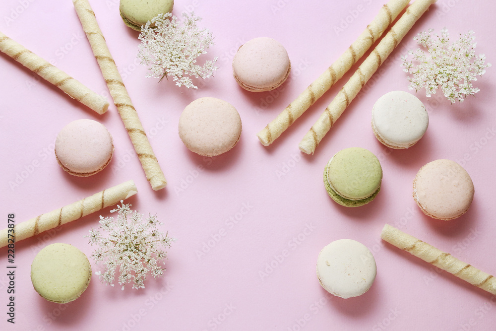 French macaroons and crispy wafer rolls on pink background. French macaroons and crispy wafer rolls on pink background.