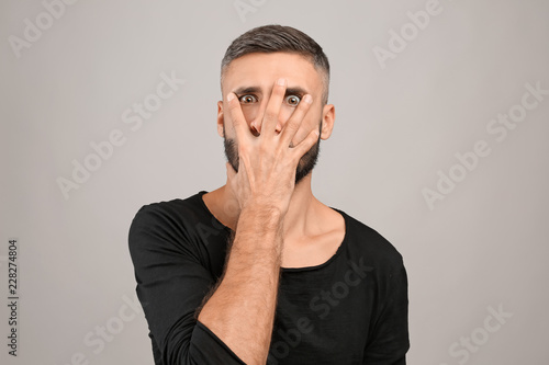 Portrait of crazy man covering face with hand on grey background