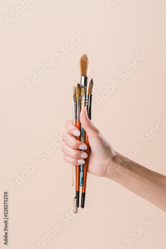 cropped shot of woman holding bunch of paint brushes isolated on beige