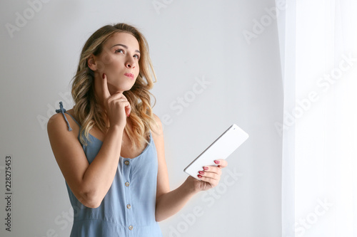 Portrait of thoughtful young woman with tablet computer on grey background