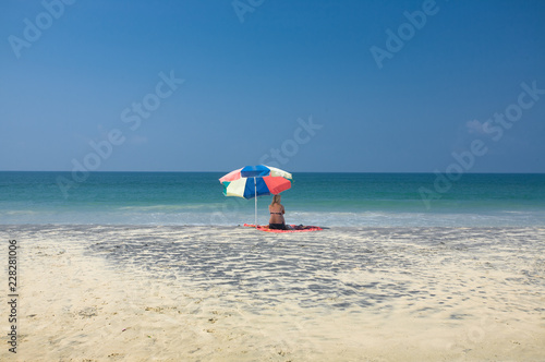 Caucasian middle aged woman sitting alone on tropical beach, looking out over the turquioise ocean.