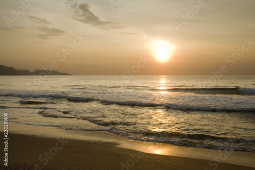 Golden orange sunset over ocean, small waves on sandy beach