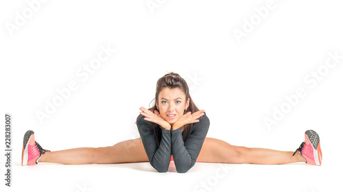 Gymnastic pose, stretch. Young adult woman doing cross-twine exercising. Studio shot, white background.