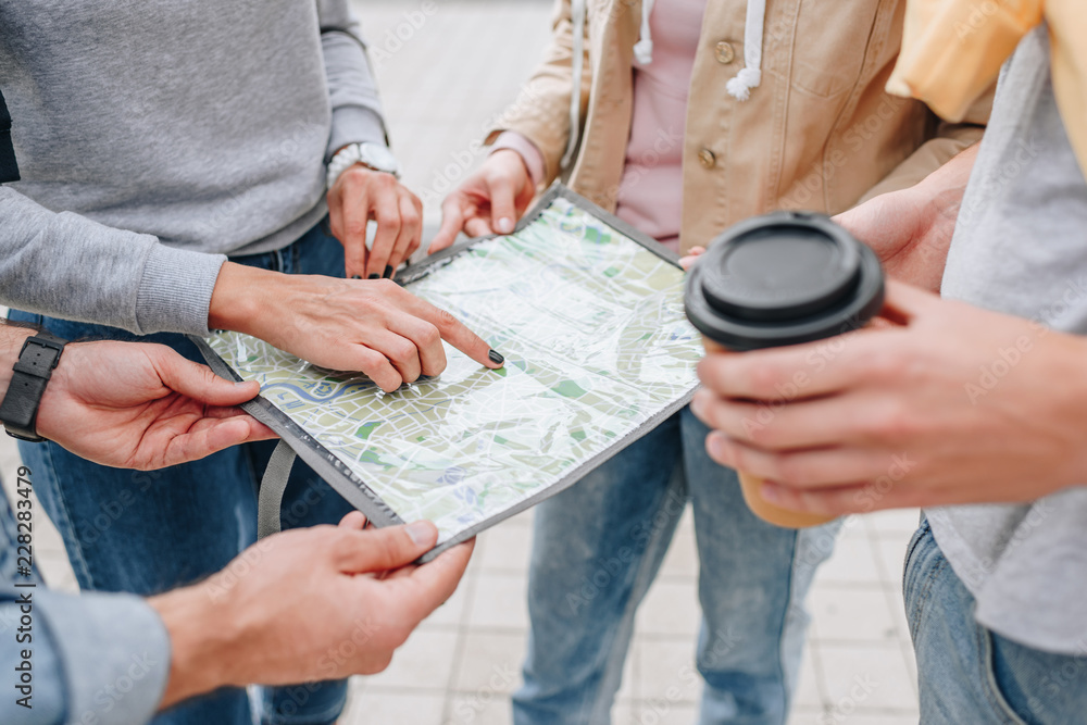 cropped view of travelers with coffee to go pointing at map in city