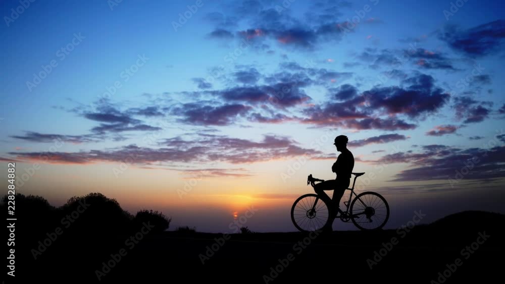 A man on a Bicycle stands on top of the mountain and admires the sunset. The camera moves on a Steadicam. A man on a Bicycle stands on top of the mountain and admires the sunset. The camera moves on a Steadicam.