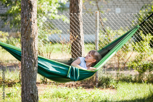 Little child girl lying in the green hammock smiling at sunny summer day on holidays outdoor in garden