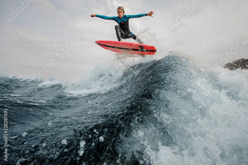 Active child boy dressed in swimsuit wakesurfing jumping up on orange board