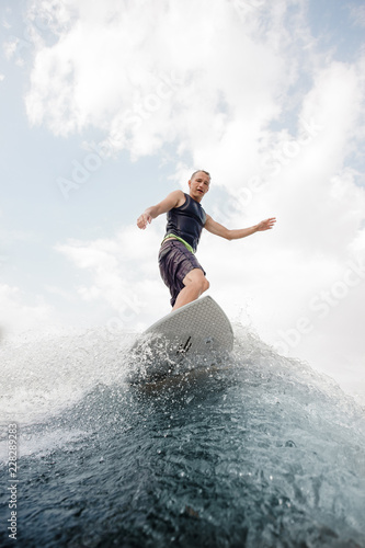 Young wakesurfer standing on the high blue wave