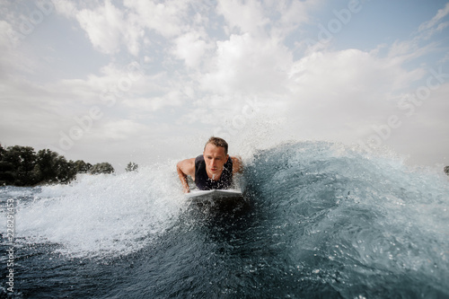 Young active man lying on the white wakeboard on the blue wave