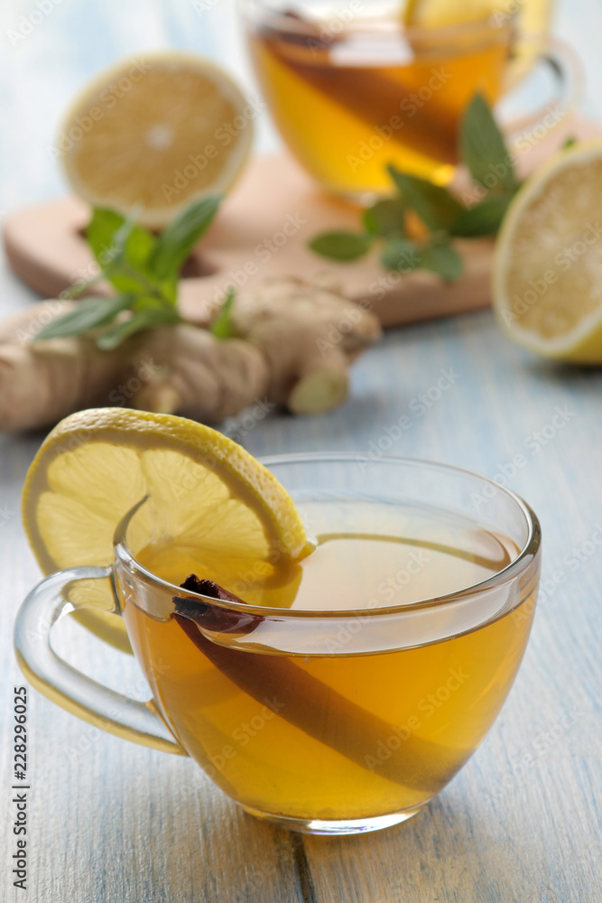 Composition with green hot tea with cinnamon, lemon and ginger on a blue wooden background Composition with green hot tea with cinnamon, lemon and ginger on a blue wooden background