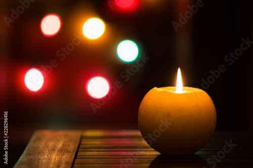 candela accesa su tavolino di legno con lucine colorate sullo sfondo, tema natale