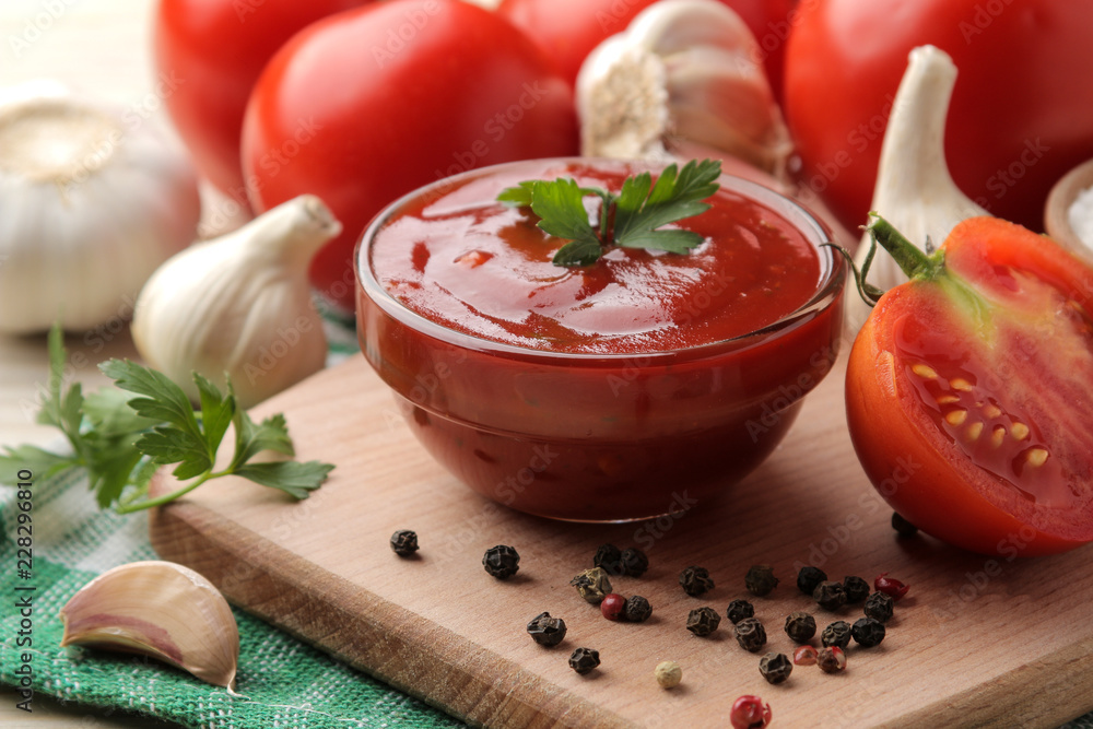 Red sauce in a bowl closeup with fresh ingredients, tomatoes, garlic and spices on a natural wooden table. Red sauce in a bowl closeup with fresh ingredients, tomatoes, garlic and spices on a natural wooden table.