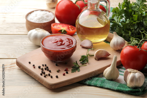 Red sauce in a bowl with fresh ingredients, tomatoes, garlic and oil and spices on a natural wooden table.