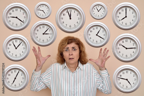 Stressed middle aged woman with a lot of clocks around her head. Each clock showing different time.