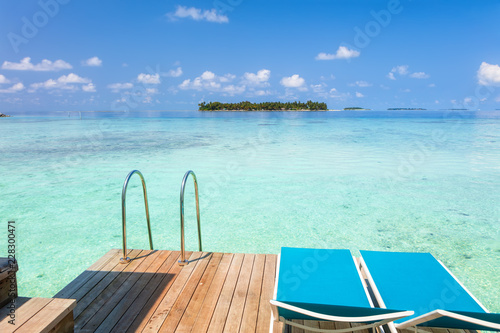 Fototapeta Naklejka Na Ścianę i Meble -  Two lounge chairs on the wooden deck with  Maldives turquoise water sea view for summer vacations holiday concept