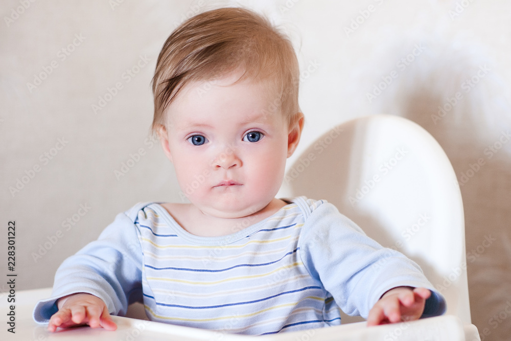Funny baby boy sitting in feeding chair in room close up. Looking at camera. Waiting for breakfast. Funny baby boy sitting in feeding chair in room close up. Looking at camera. Waiting for breakfast.