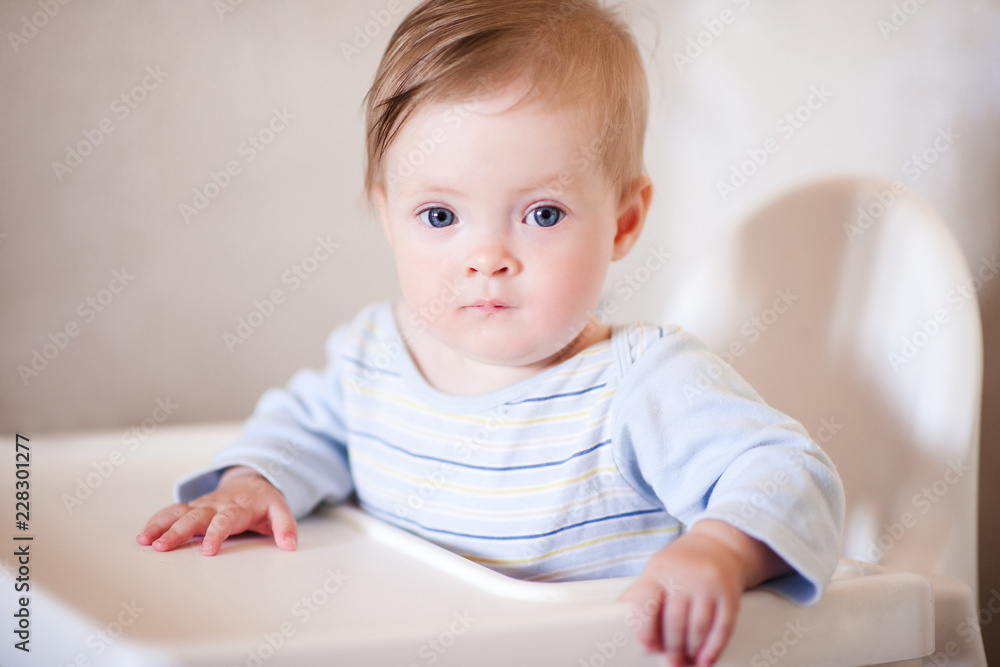 Baby girl sitting in feeding chair in room closeup. Looking at camera. Childhood. Baby girl sitting in feeding chair in room closeup. Looking at camera. Childhood.