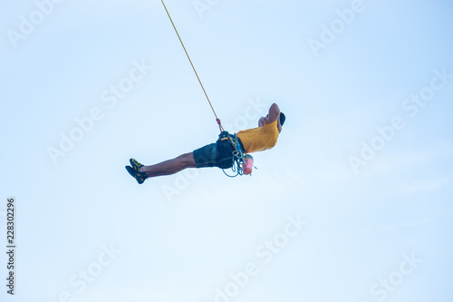 View of man without helmet hanging on a rope while rappelling and shows flying pirouettes in the air 