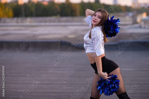 cheerleader with pompoms dancing outdoors on the roof at sunset photo