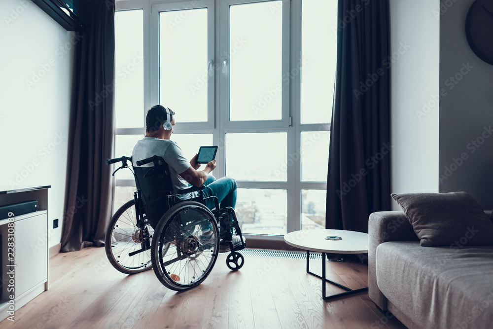 Back View Disabled Man Uses Headphones and Tablet Back View Disabled Man Uses Headphones and Tablet