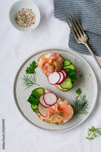 Sandwiches with smoked pink salmon  radish  cucumber and cream cheese on gray ceramic plate and textile background. Traditional Scandinavian toast. Top view.