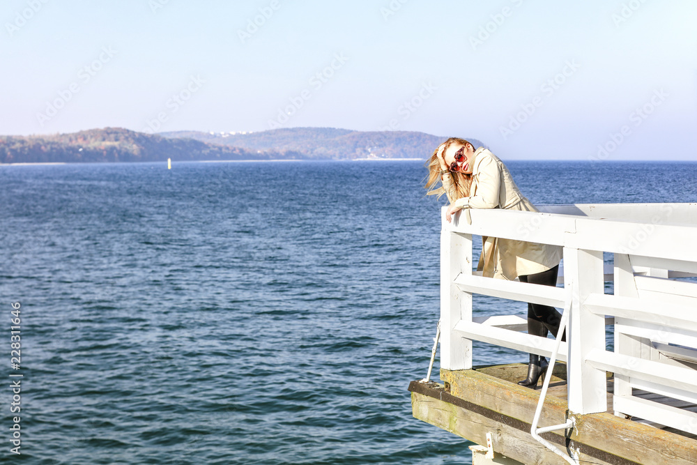 Slim young woman on wooden pier and ocean landscape. Autumn time. 