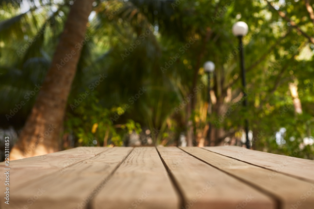 Empty top of natural wooden table for product placement and display in open shade. Coconut palm trees and green tropical plants on background. Maldives Empty top of natural wooden table for product placement and display in open shade. Coconut palm trees and green tropical plants on background. Maldives