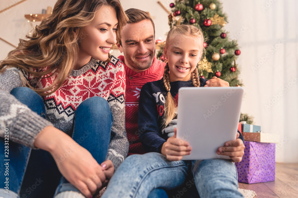 happy parents and daughter using tablet together near christmas tree at home happy parents and daughter using tablet together near christmas tree at home