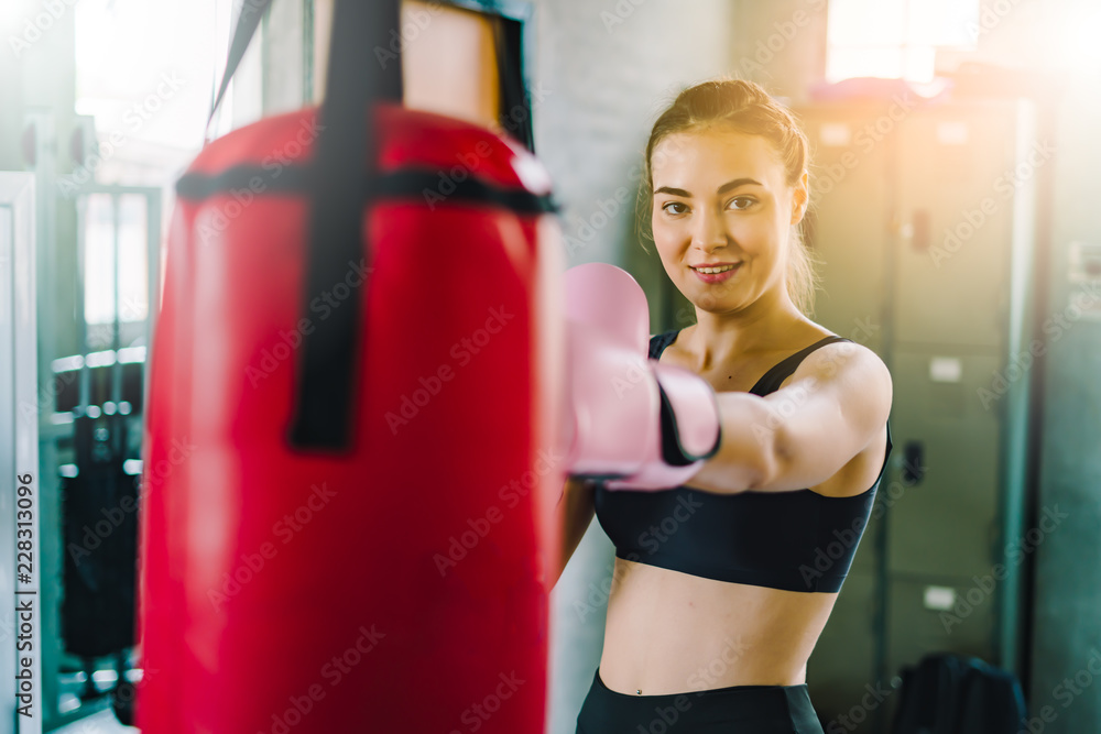 Beautiful young girl in the gym doing exercises with Boxing and smiling.young athletics girl doing dumbbells press exercises. Fitness muscled woman in black sport clothing workout on bench in gym.