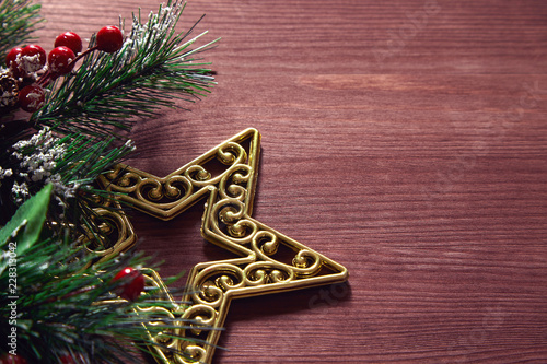 Christmas tree branches, red berries and golden decorative star on wooden background. New year backdrop.