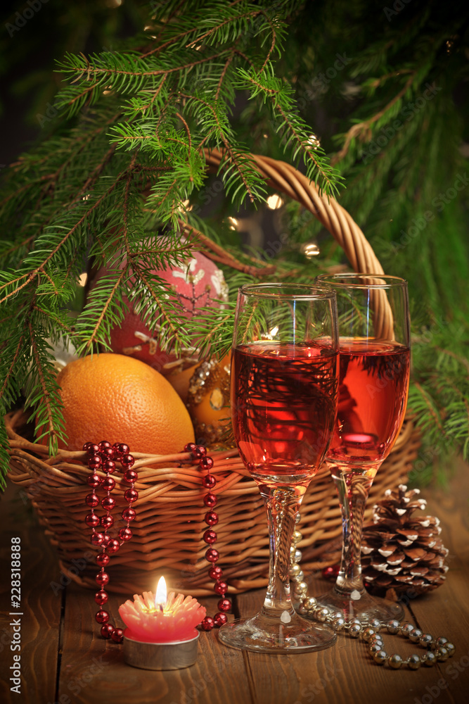 Basket with oranges and New Year toys and decoration, glasses of wine and candle in front and fir-tree on background Basket with oranges and New Year toys and decoration, glasses of wine and candle in front and fir-tree on background