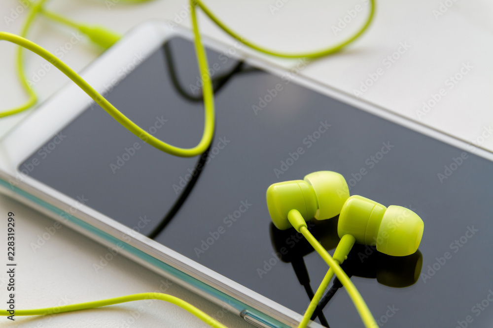 © marketlan - Modern smartphone with lime headphones on light background. Closeup, selective focus