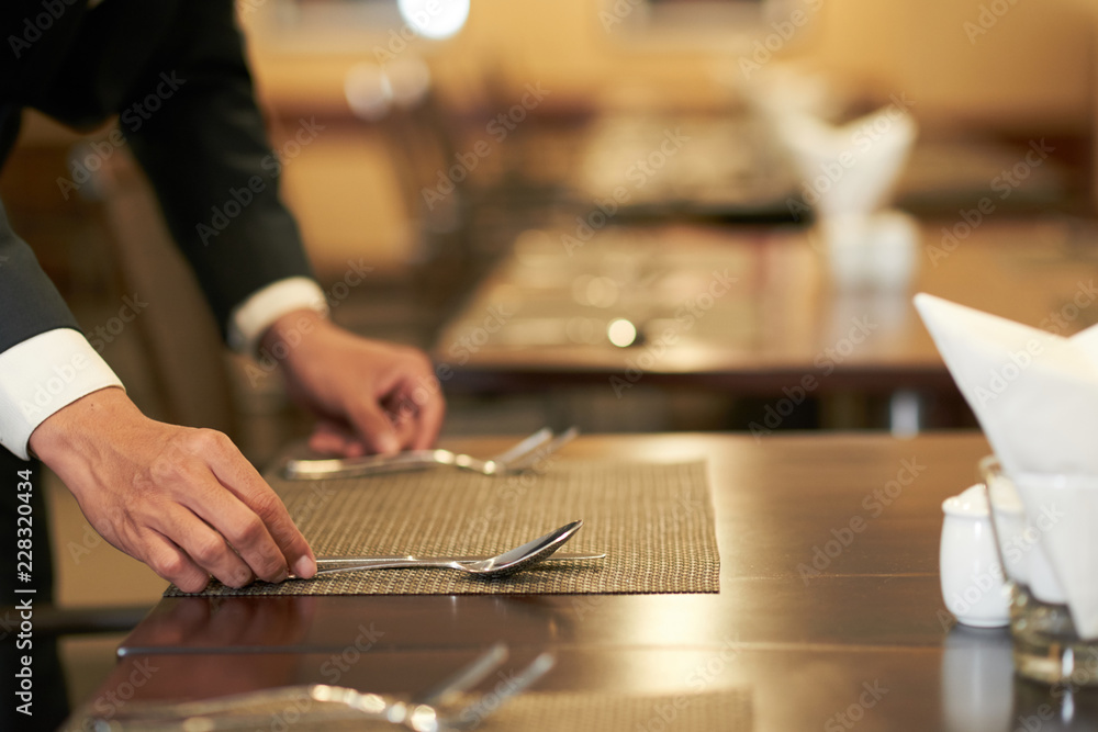 Crop elegant hotel waiter arranging silverware on napkin on table in restaurant Crop elegant hotel waiter arranging silverware on napkin on table in restaurant