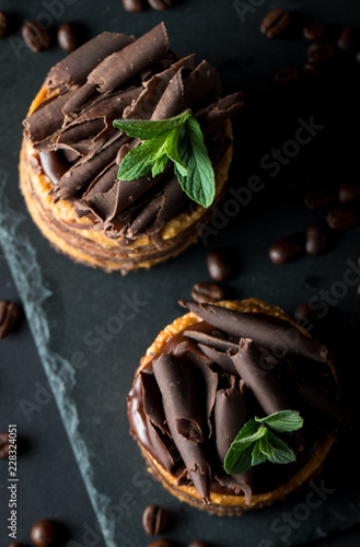 Chocolate cakes on black slatter board with mint, coffee beans on dark background, closeup photo. Fresh, tasty dessert food concept.  photo