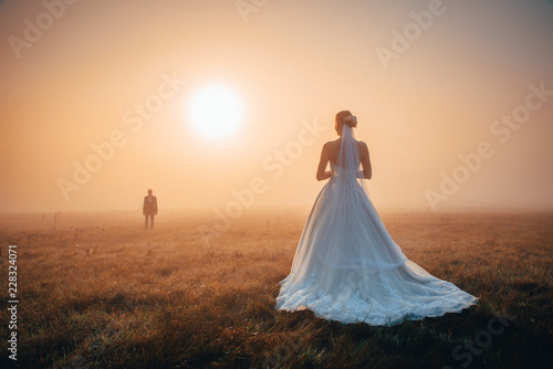 Wedding couple in autumn morning. Brdie waiting groom in orange misty sunrise light. Romantic, marriage or valentine photo. Orange edit space