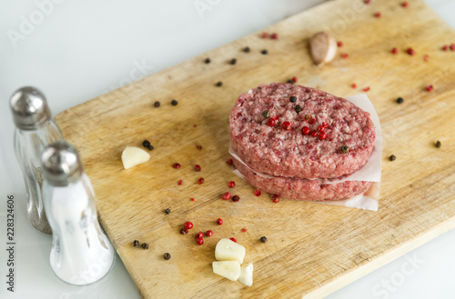 2 beef  cutlets on a wooden Board with spices, meat, garlic, pepper, salt in a salt shaker