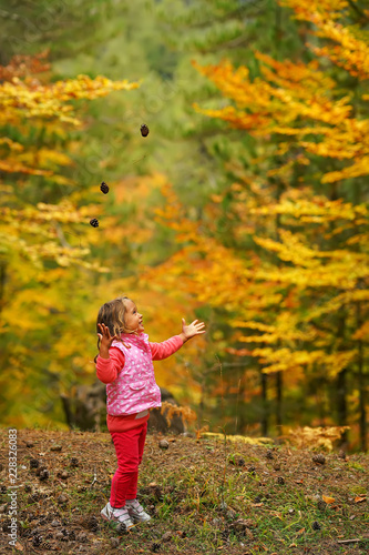 little girl in the autumn forest throws up cones