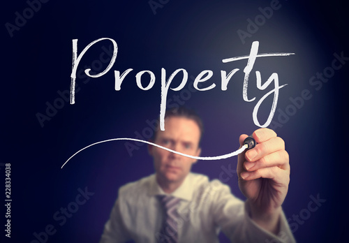 A businessman writing a Property concept with a white pen on a clear screen.