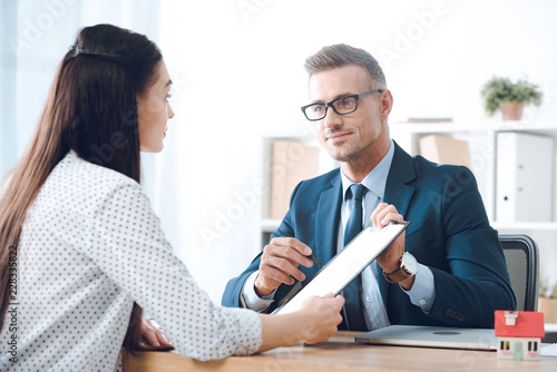 insurance agent pointing at clipboard in clients hand at tabletop in office, house insurance concept photo