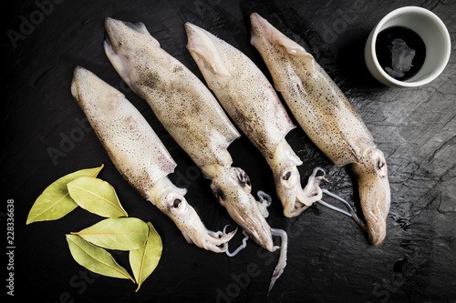 group of fresh squids next to a bowl with ink and some bay leaves photo