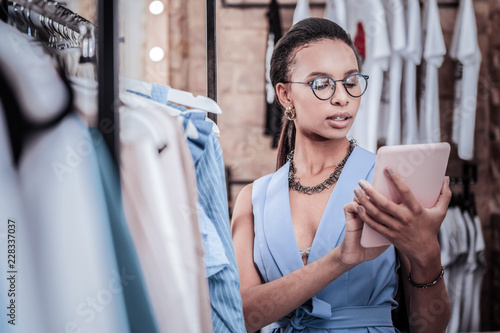 Busy woman. Busy beautiful dark-haired woman wearing elegant suit holding tablet reading e-mail standing in shop
