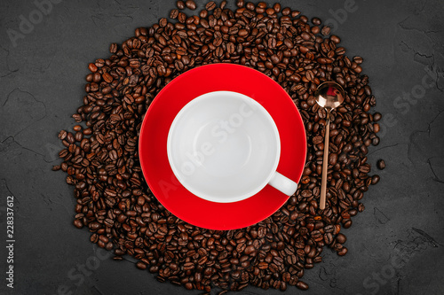 Empty white cup on the red plate with roasted coffee beans and gold spoon on the black concrete stone background. Flatlay style.
