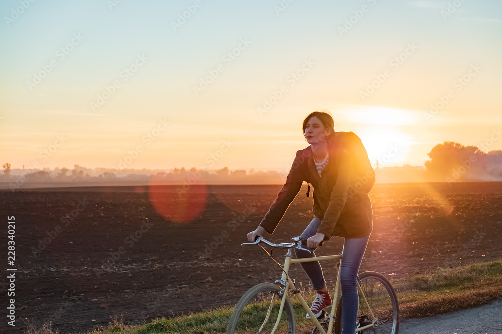 Female commuter riding a bike out of town. Woman cycling along the road at sunset