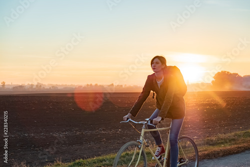 Fototapeta Naklejka Na Ścianę i Meble -  Female commuter riding a bike out of town. Woman cycling along the road at sunset