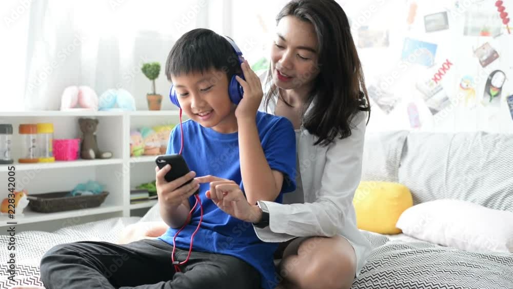 Mother and son wearing headphones using smartphone for listen to music together at home