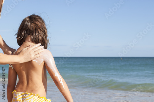 Mother applying sunblock cream to her daughter on back
