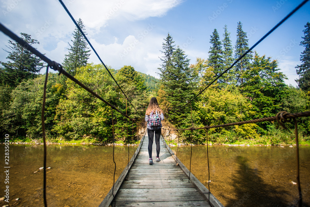 Tourist woman walk by long wooden suspension bridge above river. balance concept