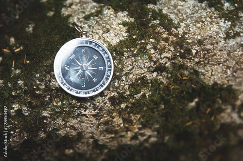 Magnetic compass with a black dial on a wild stone covered with green moss. The concept of finding the way and navigation