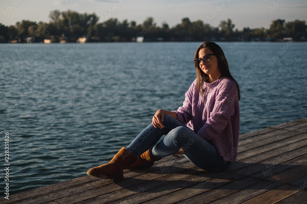 Beautiful girl with glasses sitting by the river in sunset