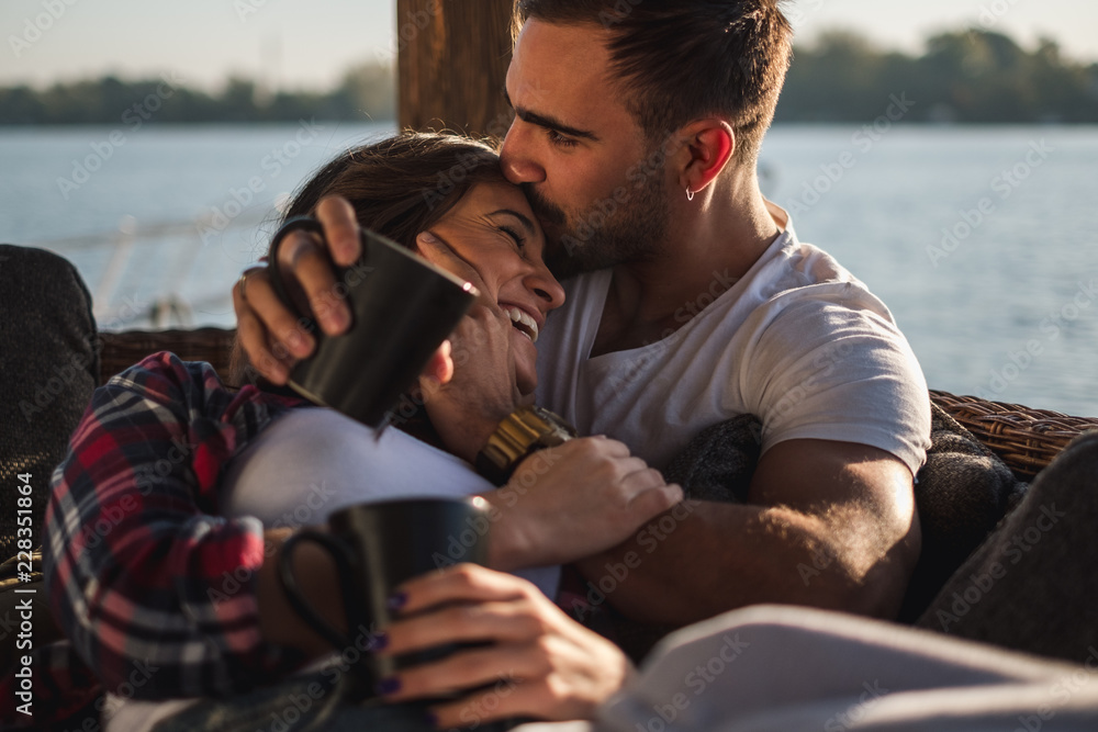 Boyfriend kissing his smiling girlfriend in forehead by the river - obrazy, fototapety, plakaty 